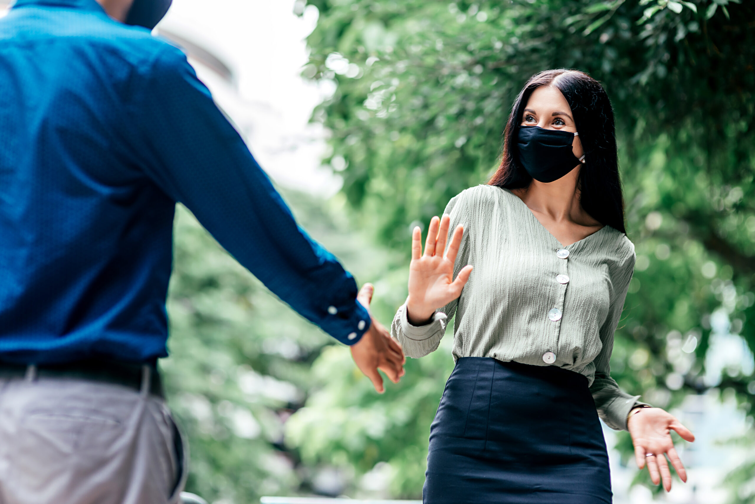 Young woman in mask refusing hand shake from a man on the street