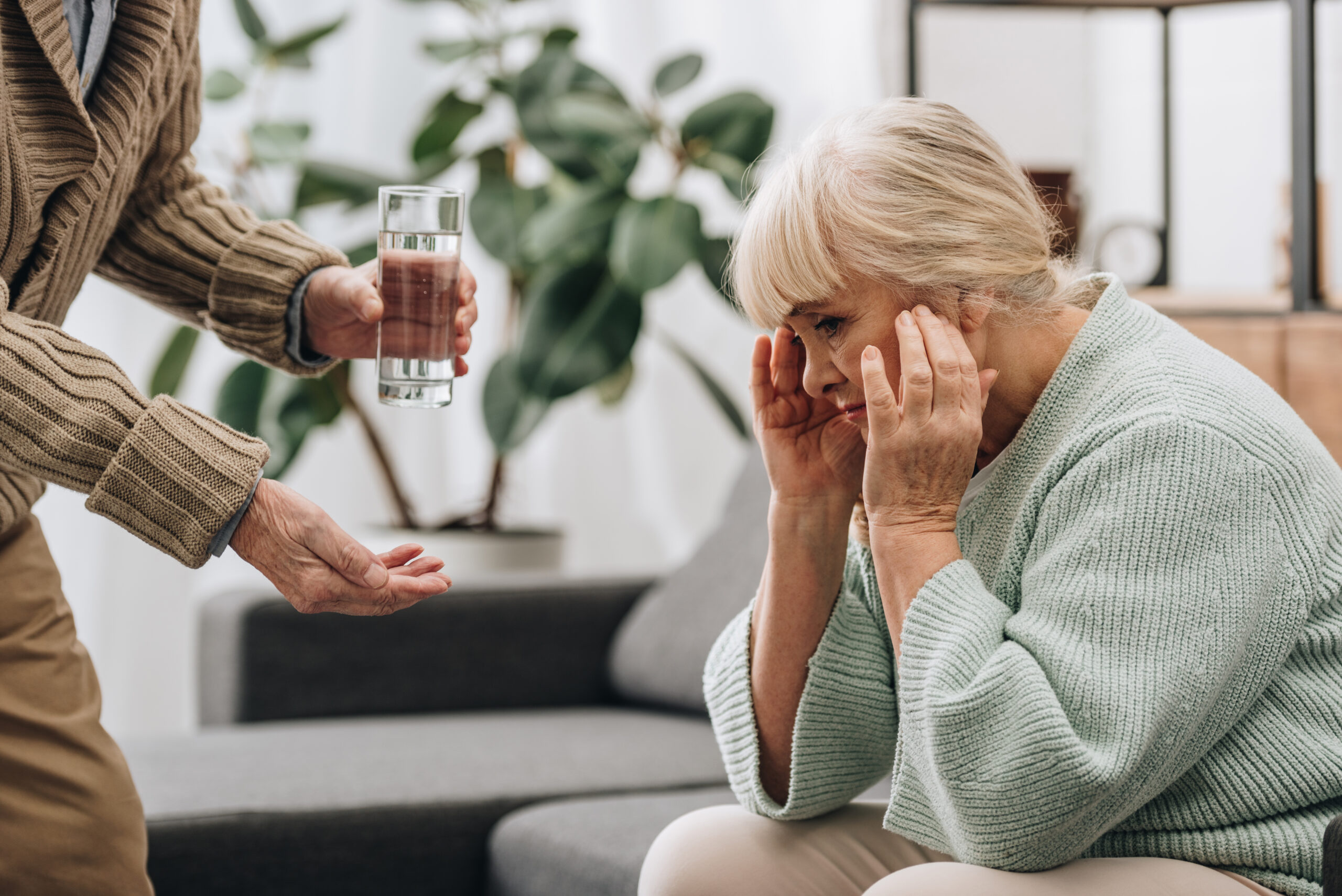 senior man giving glass of water and pills to wife